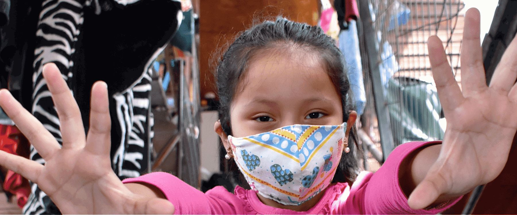 Una niña con mascarilla estampada muestra las palmas de sus manos